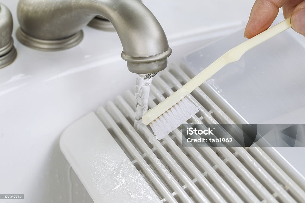 Hand cleaning fan vent cover in sink Close up horizontal photo of female hand with tooth brush cleaning bathroom fan vent cover in bathroom sink Air Duct Stock Photo