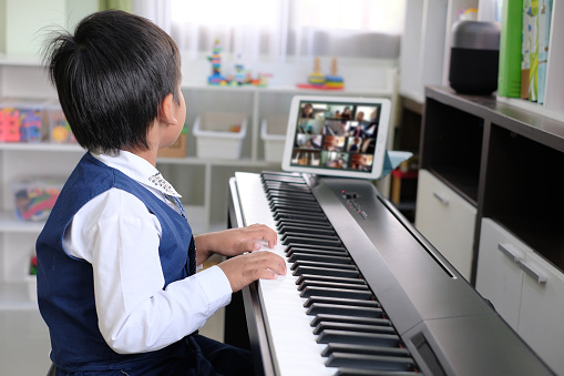 Young pianist boy looking at the digital tablet screen for learning piano online at home. Music distance learning concept.