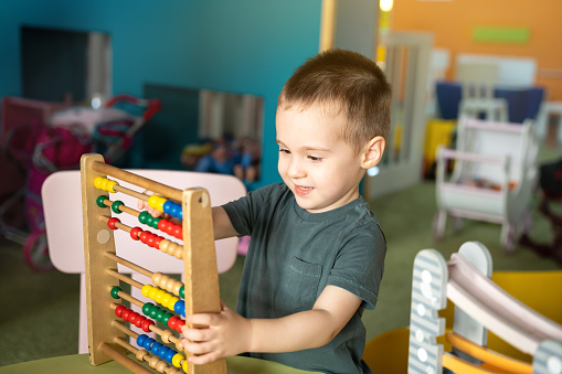 Smiling toddler boy playing with colourful toy abacus in a children's entertainment center. Educational toys for children. children's pastime