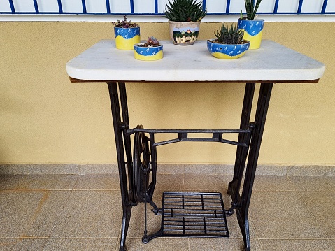 Sideboard or table made from an old iron sewing machine with a marble top and pots of succulents on a terrace. Recycling.