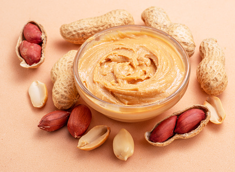Bowl of peanut butter and peanuts around it on beige background.