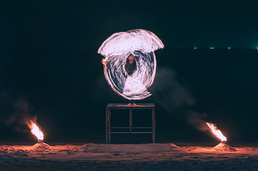 Summer Travel vacation concept, Man spinning fire steel wool with water reflection on sea in beach club party at night in Koh Samui, Thailand
