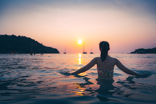 Summer travel vacation concept, Silhouette of traveler asian woman with bikini relax on sea beach at sunset in Koh Kood, Thailand