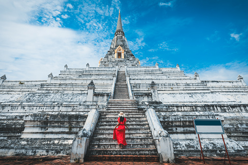 Historical local travel Thai concept, Happy traveler asian woman with dress and straw hat sightseeing in Wat Phu Khao Thong temple with white pagoda at Ayutthaya historical park, Ayutthaya, Thailand
