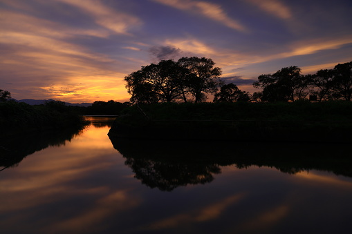 Bright dramatic golden sky at sunset with mangrove trees reflected on water surface.