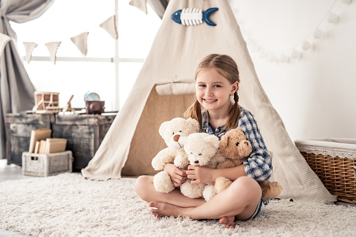 Little girl hugging plush teddies and smiling at camera in playroom