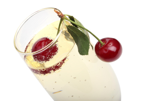 two ripe cherries into a glass with champagne, isolated on white