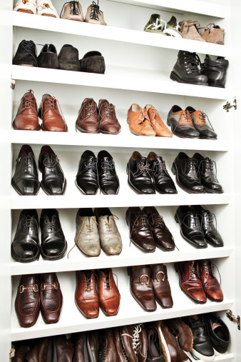A very organized shelving of man shoes in a closet.
