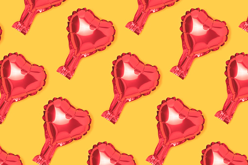 Repetitive pattern made from red heart foil balloon. Creative layout on a yellow background.