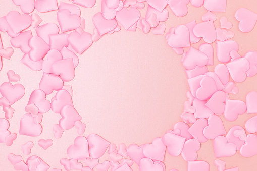 Round frame made of textile pink confetti in a heart shape on a glittering background. Monochrome concept with place for text.
