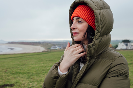 A medium close up of a young woman who is wrapped up nice and cosy in her padded jacker. She is enjoying a coastal visit to Newton by the Sea in the North East of England with her partner and their dog.