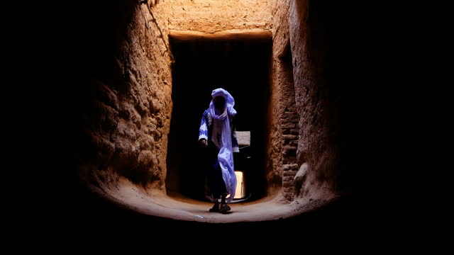 A traditional dressed Bedouin Moroccan man wearing a blue gandoura and a turban walks inside the Kasbah in Mhmaid, Morocco.