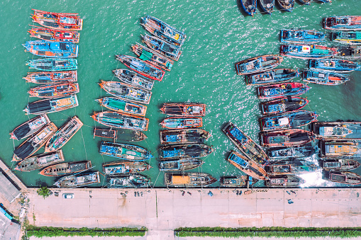 Fishing boats from above anchored at Songkhla Harbour on a beautiful blue water. Aerial top view of fishing boats with copy space for text.