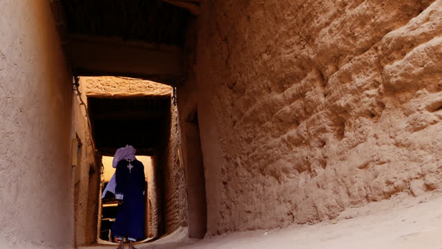 A traditional dressed Bedouin Moroccan man wearing a blue gandoura and a turban walks inside the Kasbah in Mhmaid, Morocco.