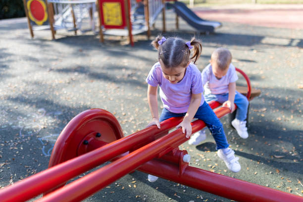 menina e menino bonitos na gangorra. playground público e conceito de infância. - swinging sister family child - fotografias e filmes do acervo