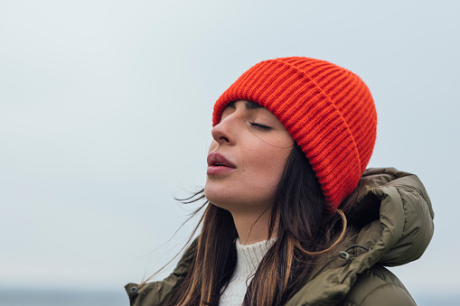 A medium close up of a young woman enjoying a coastal. She is having a mindful moment and doing some breathing exercises and closing her eyes and feeling the sea air on her face. She is in Newton by the Sea in the North East of England.