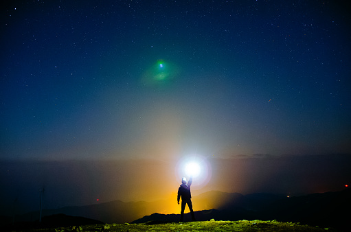 A person holding a flashlight under the starry sky