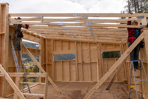 Two construction workers attach roof trusses