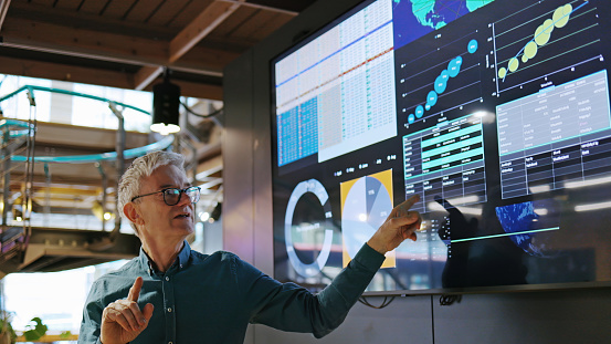 Stock image of a mature man conducting a seminar / lecture with the aid of a large screen. The screen is displaying graphs & data associated with the earth.
