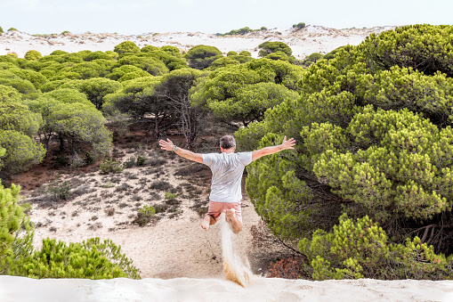 Man jumping on the sand of a dune with trees in the background. Concept of freedom