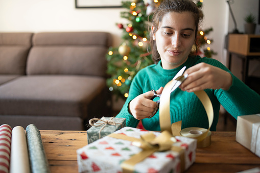 Young woman wrapping up the Christrmas presents.She is using wrapping paper and ribbon.