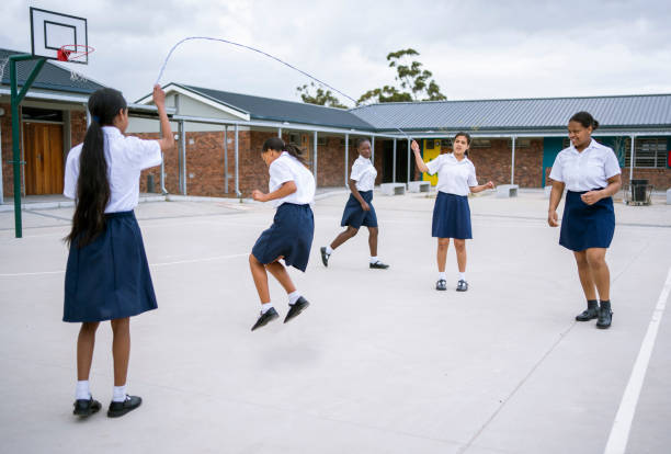 School children playing jump rope game in school yard during recess Group of school children playing jump rope game in school yard during recess trans boy stock pictures, royalty-free photos & images