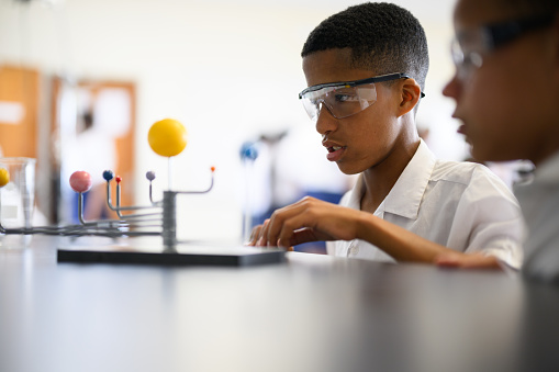 Schoolboys wearing protective glasses in science class building solar system model