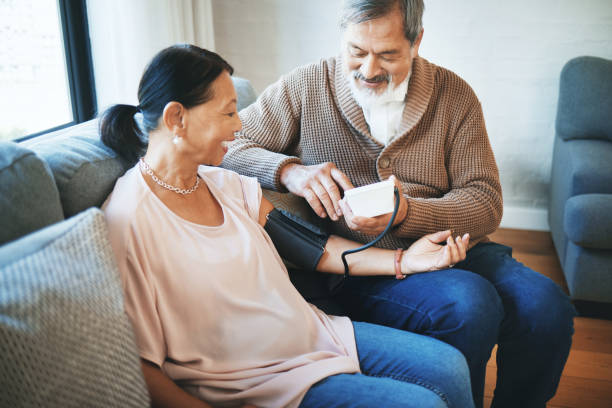 presión arterial, atención médica y pareja de ancianos en sala de estar con equipo para hipertensión. hombre enfermo, amor y anciano con herramienta médica para la mujer en la jubilación en el salón de la casa moderna juntos - patience blood pressure gauge physical pressure nurse fotografías e imágenes de stock