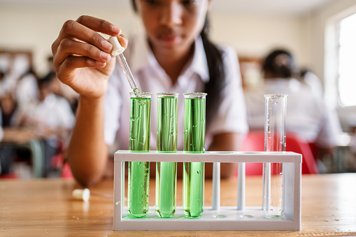 Close-up of a schoolgirl carefully dropping a chemical using dropper into a test tube in science class