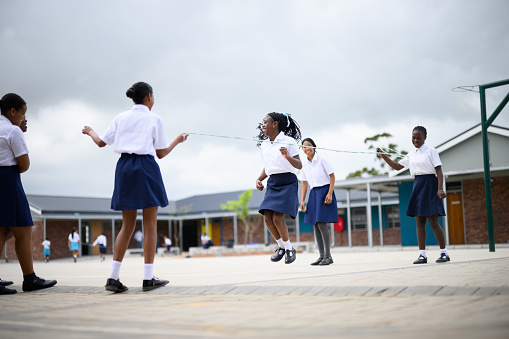 Schoolgirl in midair skipping with friends in school courtyard