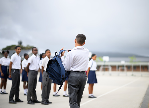 Back view schoolboy swings rucksack onto back lining up for first day back at school