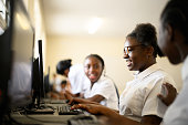 Friends smile as schoolgirl gets it right working on desktop computers in classroom