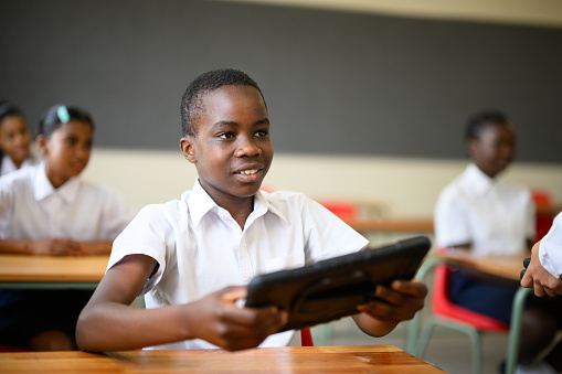 Candid portrait young African boy holding digital tablet in classroom