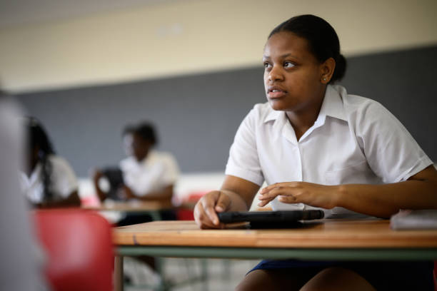 Student concentrates using digital tablet and listening to teacher in classroom