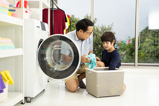 Happy family man father householder and child son little helper are having fun and smiling while doing laundry with washing machine