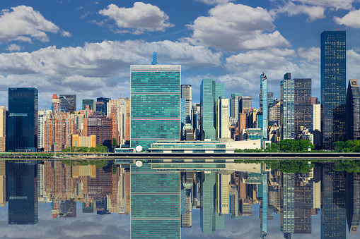 High Resolution Stitched Image of New York Skyline with UN Building (Headquarters of the United Nations), Manhattan Upper East Side Residential and Office High-rises, FDR drive, Green Trees and Morning Blue Sky with Clouds all Reflected in water of East River. Canon EOS 6D (Full Frame censor) DSLR and Canon EF 85mm f/1.8 Prime lens. 3;2 Image Aspect Ratio. This image is downsized to 50MP.