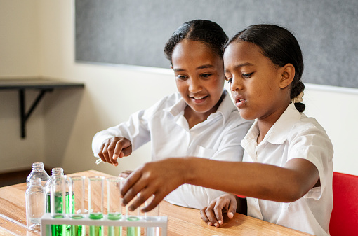 Two girl students sitting at table in science class doing experiment with chemicals in school