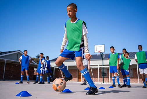 School soccer team training outdoors with a boy leading ball between cones in schoolyard