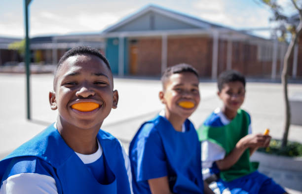 Schoolboys soccer players wearing orange peel as mouth guard sitting on bench Funny schoolboys in soccer uniform wearing orange peel as mouth guard while sitting on bench on school playground oranges with faces stock pictures, royalty-free photos & images