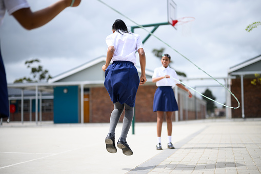 Schoolgirls skipping together in playground at school.
