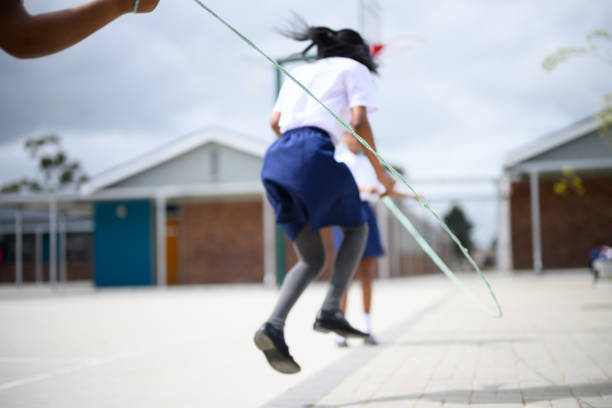 Schoolgirls skipping together in playground at school.