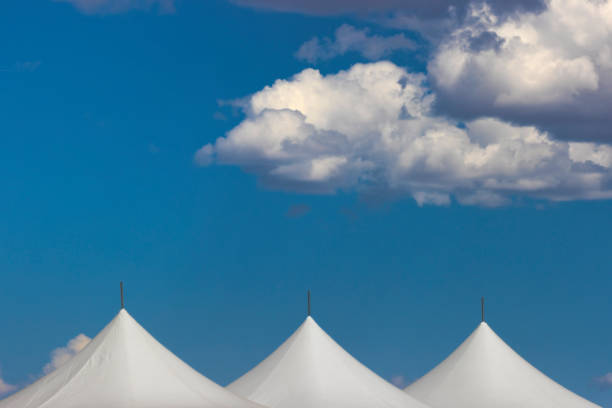 istock Clouds float over the tops of white tents in blue sky. 1770739187