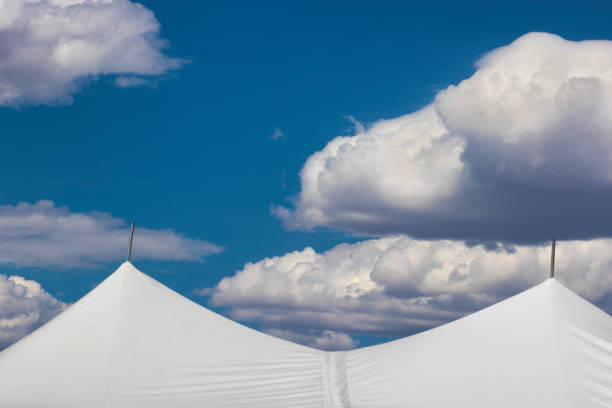 istock Clouds float over the tops of white tents in blue sky. 1770741056