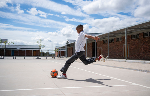 Teenage boy in school uniform kicking a football in school playground