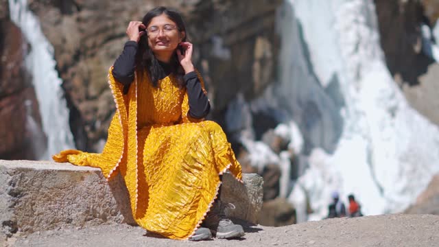 Beautiful Indian woman sitting on the background of a frozen waterfall in Spiti Valley, India. Winter Spiti. Female relaxing near scenic winter location.