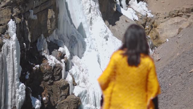 Defocused tourist woman looking at frozen waterfall during winter in Spiti Valley, Himachal Pradesh, India. Winter scene in north India.