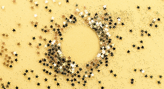 Gold Stars and Sparkles form a Ring for Copy Space on Yellow Background.
