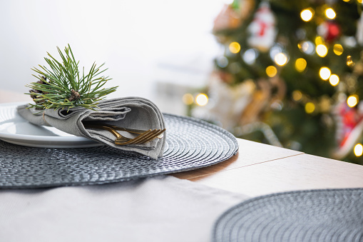 Serving a festive table with plates, forks, knives, napkins close-up tissue in a cage decorated for Christmas and New Year pine branch with a cone. Eco-style, minimalism