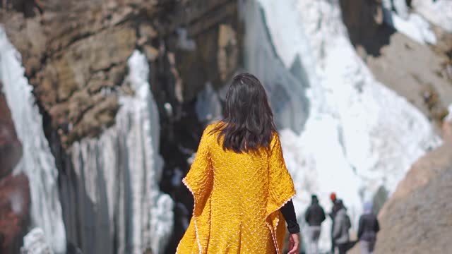 Rear view of Indian girl walking near frozen Lingti waterfall in Spiti Valley, India. Frozen waterfall during winter in Spiti. Travel and holiday concept.