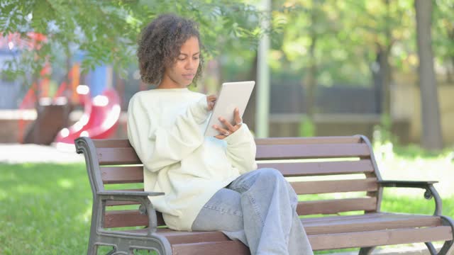 Young African Woman using Tablet while Sitting Outdoor on a Bench